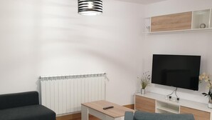 A modern living room with a flat-screen TV, two sofas, a coffee table, and a radiator. - Modern Apartment for 6 in Jaca Center, Near Cathedral (Jaca)