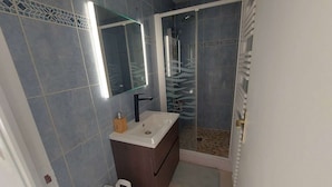 Ein Badezimmer mit weißem Waschbecken, dunklem Holzschrank und einer Duschkabine aus Glas.