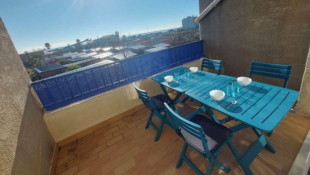 Ein Balkon mit blauem Tisch und Stühlen, Blick auf die Stadt und strahlend blauer Himmel.