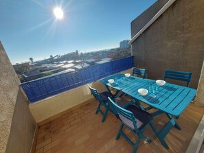 Varanda com mesa e cadeiras azuis, vista da cidade e céu claro.