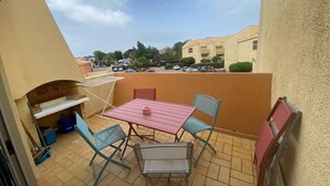 Une petite terrasse extérieure avec une table et des chaises, un barbecue et une vue sur un quartier résidentiel.