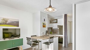 Une cuisine moderne dotée d’un îlot central, de tabourets de bar, d’une table à manger et d’un téléviseur.