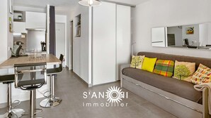 Un appartement moderne doté d’une kitchenette, d’un coin repas avec des tabourets de bar, d’un canapé agrémenté de coussins colorés et d’un grand miroir mural.