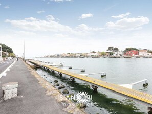 Une promenade en bord de mer avec un pont piétonnier jaune, une eau calme et des bâtiments en arrière-plan.