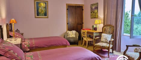 A room with two beds, a desk, and a chair. There is a window with curtains, a lamp, and a painting on the wall.