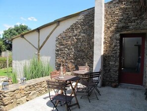 A stone building with a door, a table with chairs, and a small garden area. - Rustic Getaway: Cozy Room, Private Bath, Breakfast, and Family Friendly in Bouvron (Bouvron)