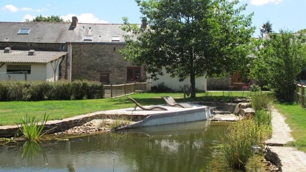 A pond with a small boat, surrounded by a grassy area and a building with a sloped roof. - Rustic Getaway: Cozy Room, Private Bath, Breakfast, and Family Friendly in Bouvron (Bouvron)