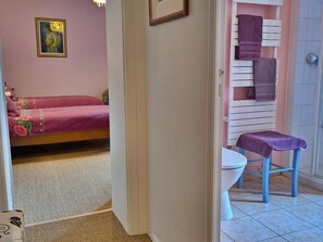 A bedroom with a bed, a bathroom with a toilet and a shower, and a hallway.