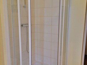 Un box de ducha con puerta de cristal, ducha y paredes de azulejos.