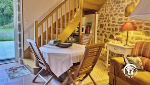 Una habitación acogedora con una escalera de madera, una mesa de comedor con sillas, un sofá y una lámpara.