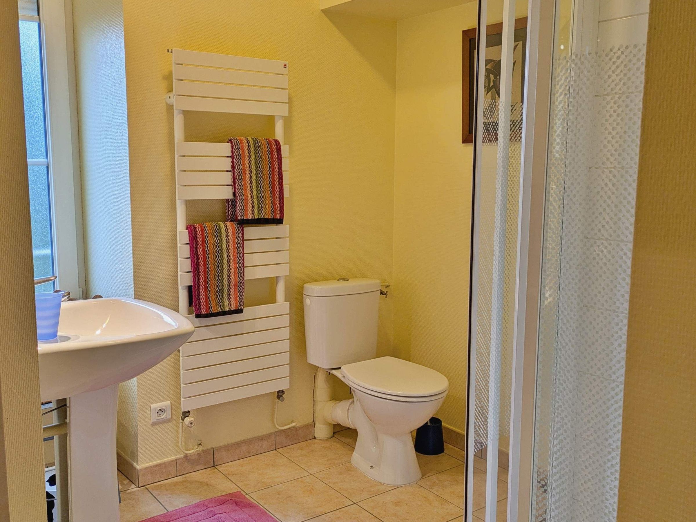 Une salle de bain comprenant des toilettes, un lavabo, un porte-serviettes avec des serviettes colorées et un espace douche.
