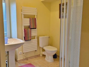 A bathroom with a toilet, a sink, a towel rack with colorful towels, and a shower area.