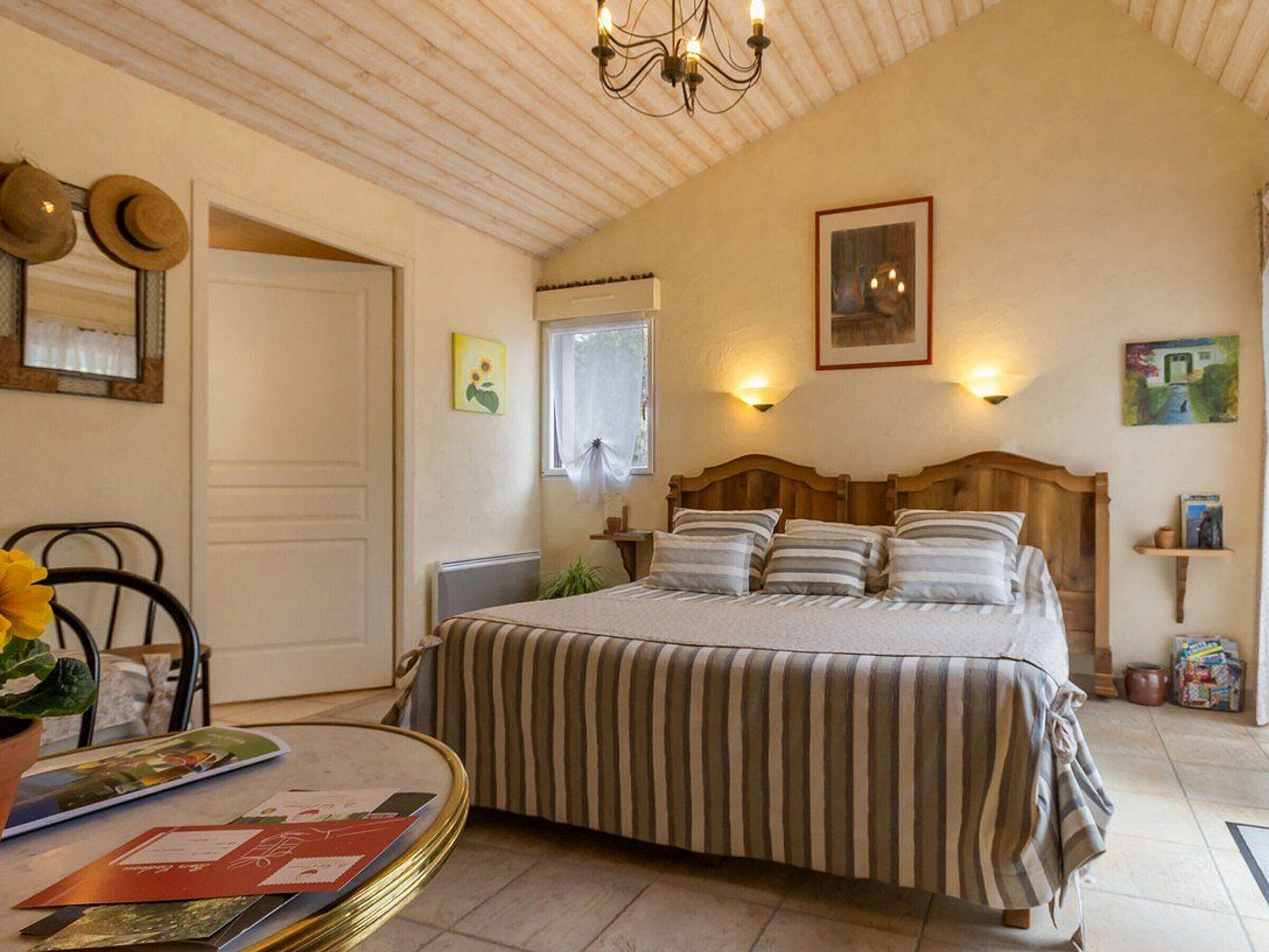 Un dormitorio con una cama grande, un cabecero de madera, una mesita de noche con lámpara, una silla y una ventana con cortinas.