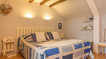 A bedroom with a wooden ceiling, a bed with a blue and white striped bedspread, a bedside table with a lamp, and a wall-mounted shelf with decorative items.