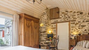 A bedroom with a stone wall, wooden wardrobe, bed, and a small table with a lamp. - Room with air conditioning - 2 guests (Blain)