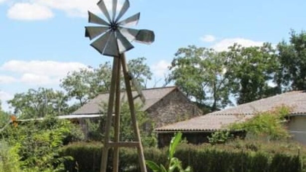 A windmill in a garden with a pond, surrounded by greenery and a house in the background. - Rustic Charm in Bouvron: Cozy Room, Private Ensuite, Child-Friendly Amenities & Fireplace Breakfast (Bouvron)