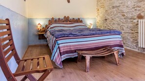 A bedroom with a wooden bed, a wooden chair, a stone wall, and a nightstand with a lamp. - Rustic Charm in Bouvron: Cozy Room, Private Ensuite, Child-Friendly Amenities & Fireplace Breakfast (Bouvron)