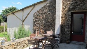 A stone building with a door, a table with chairs, and a small garden area. - Rustic Charm in Bouvron: Cozy Room, Private Ensuite, Child-Friendly Amenities & Fireplace Breakfast (Bouvron)