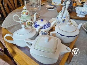 Una mesa con varios teteras y tazas, algunas con motivos florales, y una jarra de vidrio.