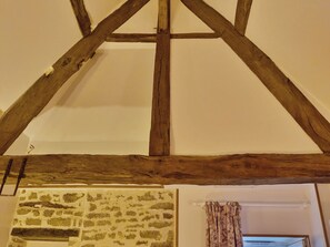 Una habitación con vigas de madera a la vista, una pared de piedra y una ventana con cortinas florales.