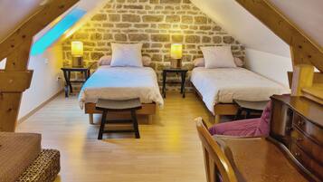 A cozy attic bedroom with two beds, wooden floors, stone walls, and a sloped ceiling.