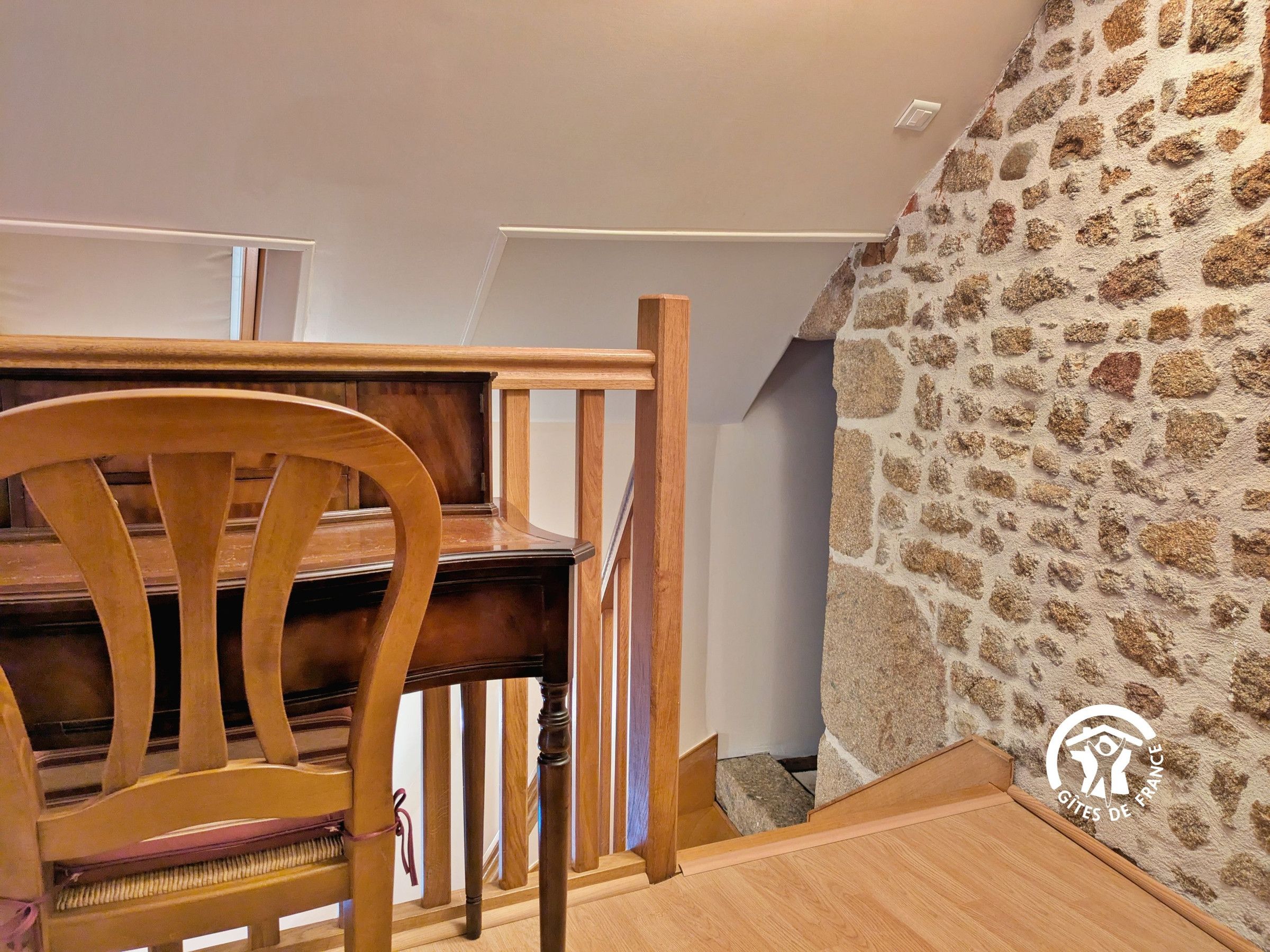 Un piano en bois dans une pièce dont un mur est en pierre et qui possède un escalier en bois.
