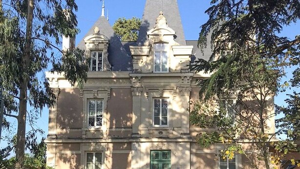 Un edificio grande y antiguo con fachada simétrica, numerosas ventanas y una puerta verde destacada.