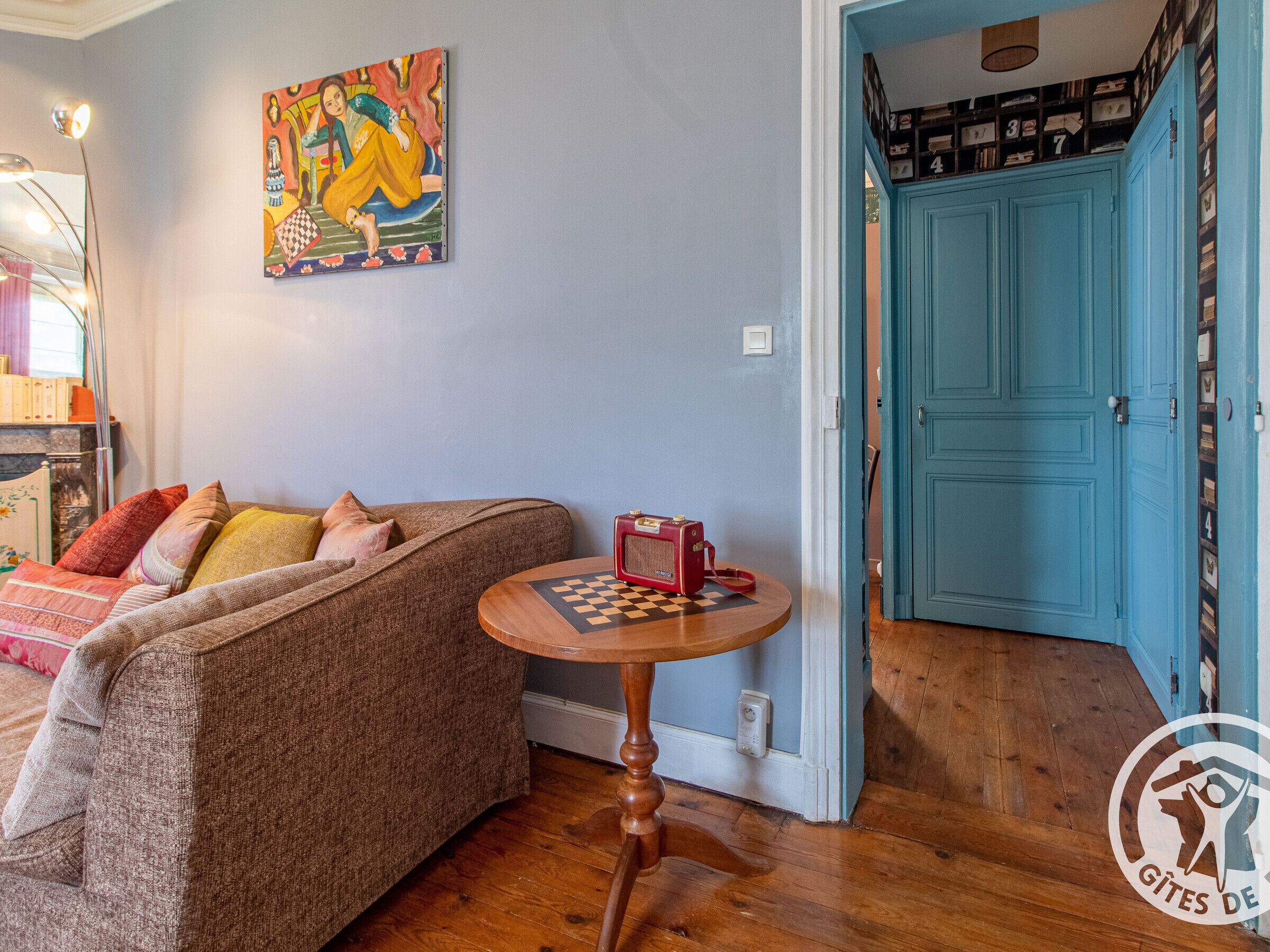 A cozy living room with a sofa, a small table with a chessboard, and a blue door leading to a storage area.