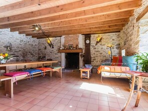 Een rustiek interieur met zichtbare stenen muren, houten balken, een open haard en een eetgedeelte met banken en tafels.