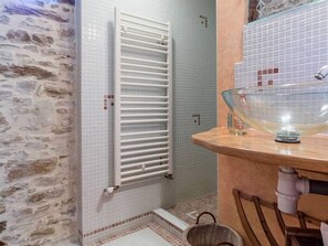 Een badkamer met een stenen muur, een witte radiator, een glazen schaal op een houten aanrecht en een betegelde vloer.