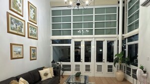 Ein geräumiges Wohnzimmer mit großem Fenster, einer Kandelaberleuchte und einem schwarzen Ledersofa.