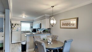 A modern kitchen with white cabinets, a central island, and a dining area with a round table and four chairs. - Villas on the Gulf #D3 | Quick Beach Access & Local Fun (Pensacola Beach)