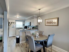 A modern kitchen with white cabinets, a central island, and a dining area with a round table and four chairs. - Villas on the Gulf #D3 | Quick Beach Access & Local Fun (Pensacola Beach)