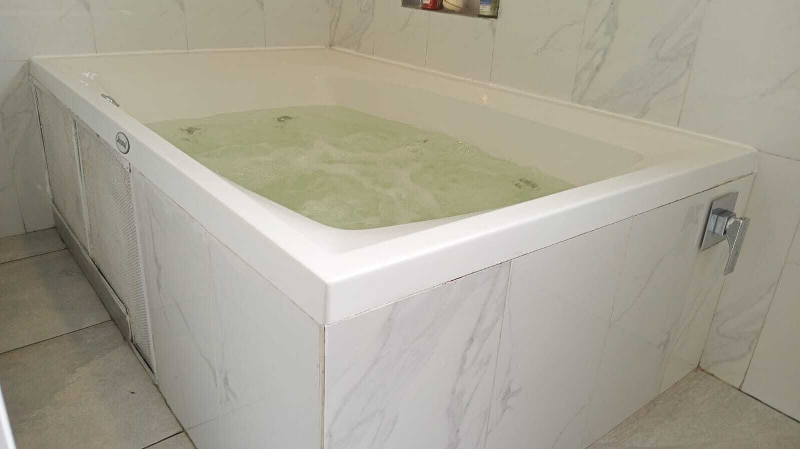 Une baignoire blanche dont l’eau a une teinte verdâtre, un pommeau de douche et un panneau de commande fixé au mur.