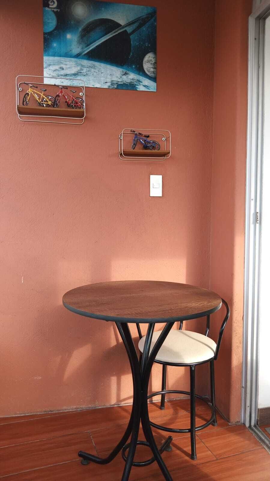 A small round table with a chair, a wall-mounted light switch, and a framed picture of a space scene.