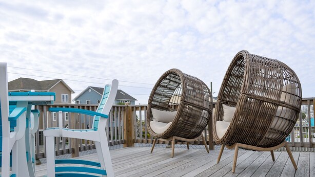 Una terraza de madera con sillas de mimbre y una silla blanca con detalles azules.