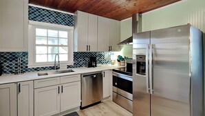 Una cocina moderna con armarios blancos, electrodomésticos de acero inoxidable y techo de madera.