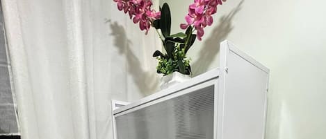 A white metal shelving unit with three glass doors, a blue water dispenser, and pink flowers on top.