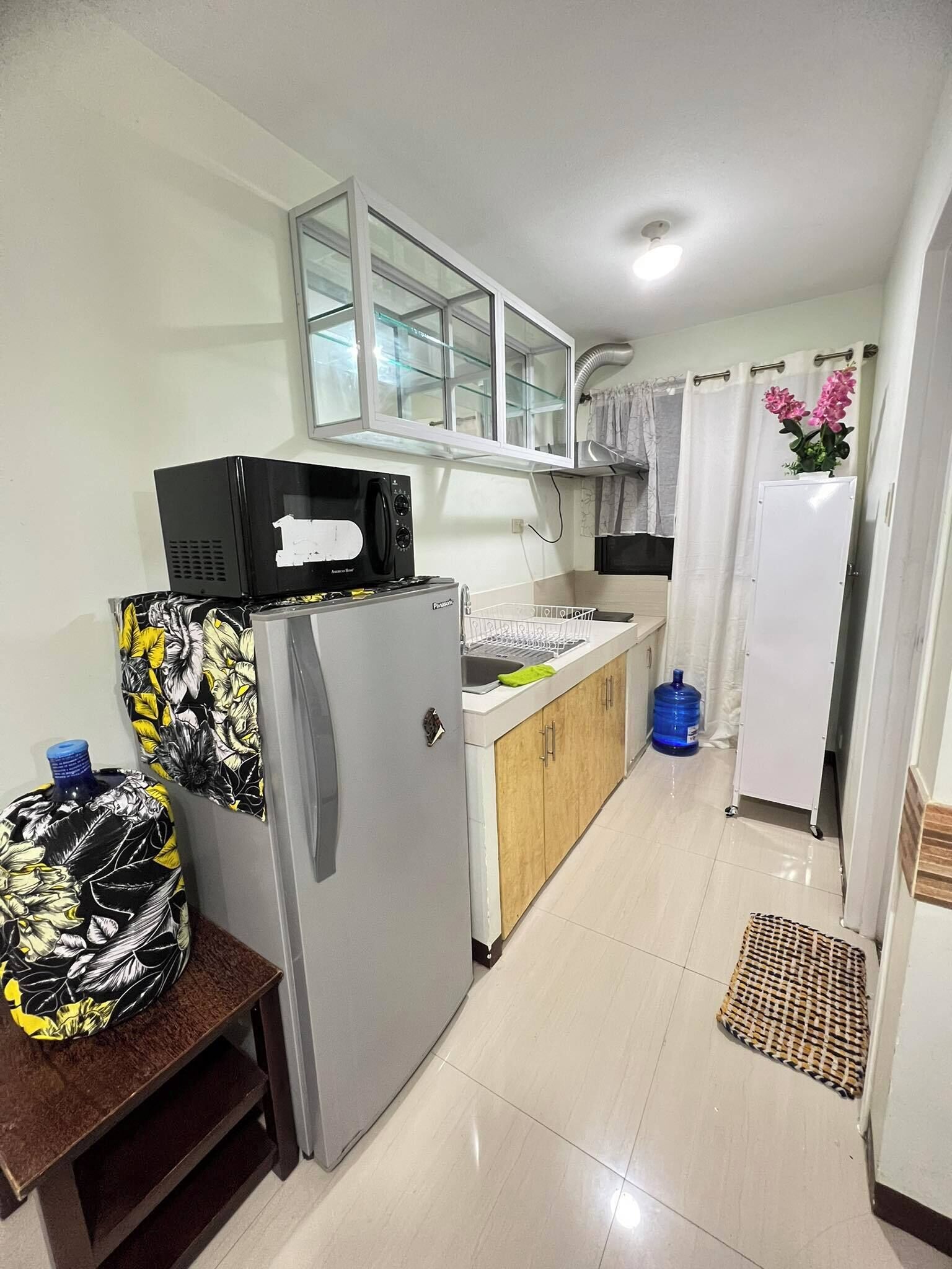 A compact kitchen with a refrigerator, microwave, and a small sink. There is a water dispenser and a large water bottle on the counter.