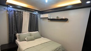 A bedroom with a bed, a nightstand, a wall-mounted air conditioner, and a ceiling light fixture. - One Oasis Condo 2 BR Near SM City Davao (Davao)