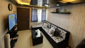 A living room with a sofa, coffee table, TV, and a wall-mounted shelf with flowers. - One Oasis Condo 2 BR Near SM City Davao (Davao)