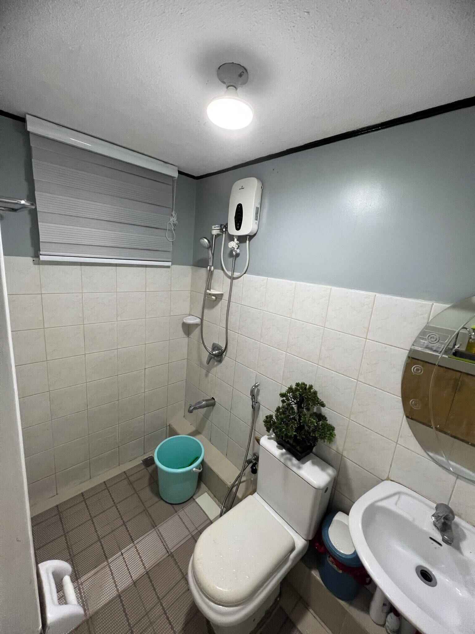 A small bathroom with a toilet, sink, shower, and a window with blinds.