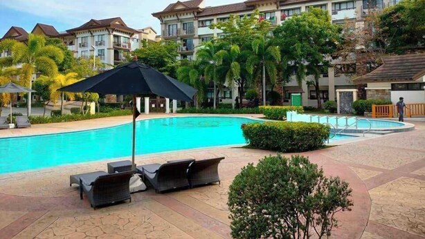 A hotel with a swimming pool, lounge chairs, and a covered area with an umbrella. - One Oasis Condo 2 BR Near SM City Davao (Davao)