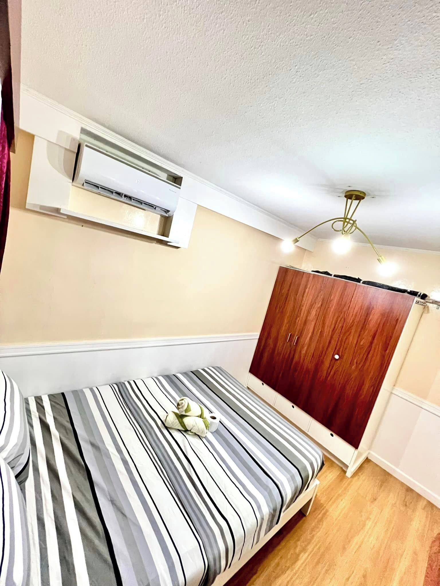 A bedroom with a bed, a wardrobe, an air conditioning unit, and a ceiling light fixture.