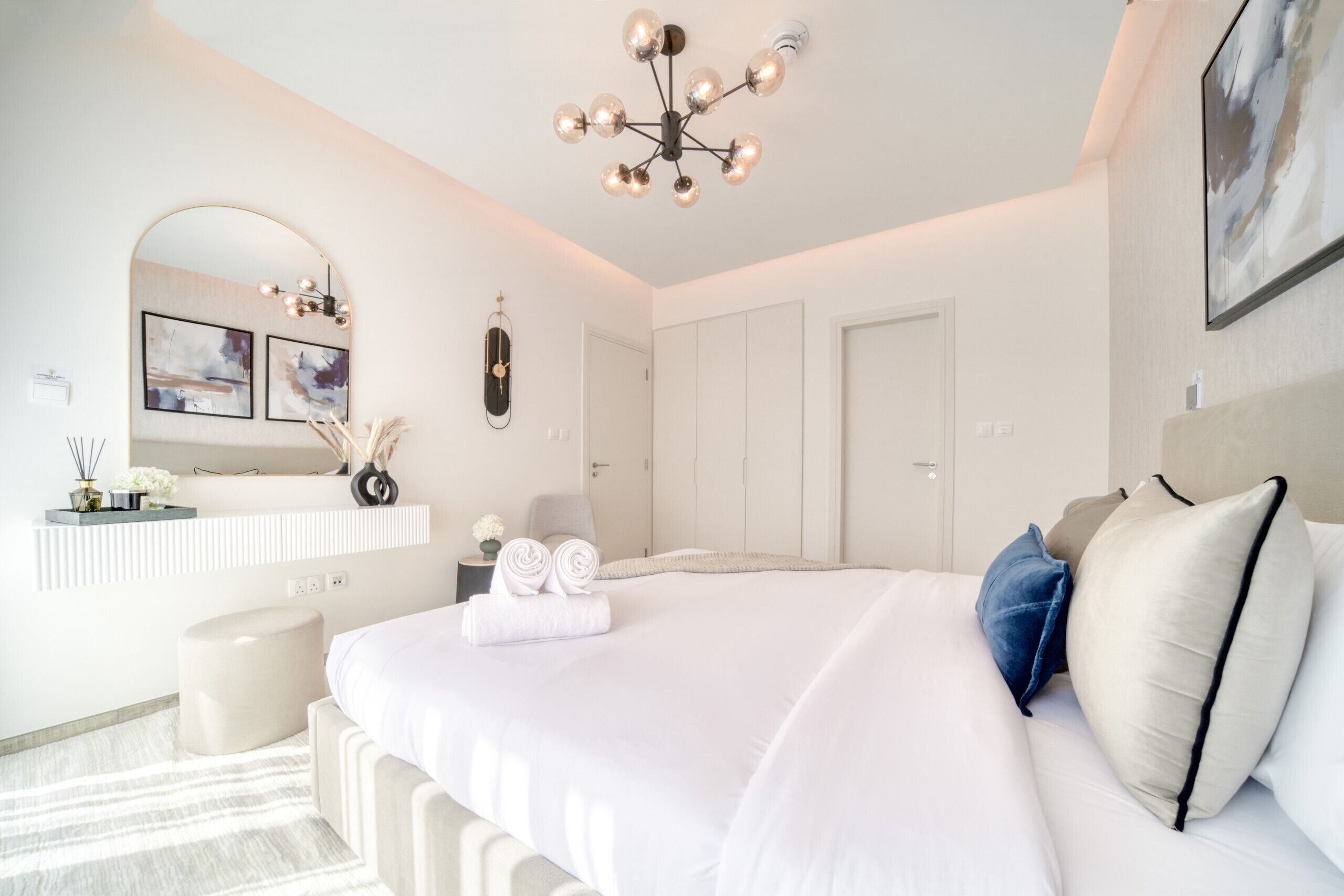 Een moderne slaapkamer met een groot bed, een kaptafel met spiegel en een plafondlamp.