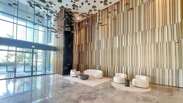 Un hall d’entrée spacieux avec un sol en marbre poli, un coin salon doté de canapés blancs et un mur revêtu de panneaux de bois verticaux.