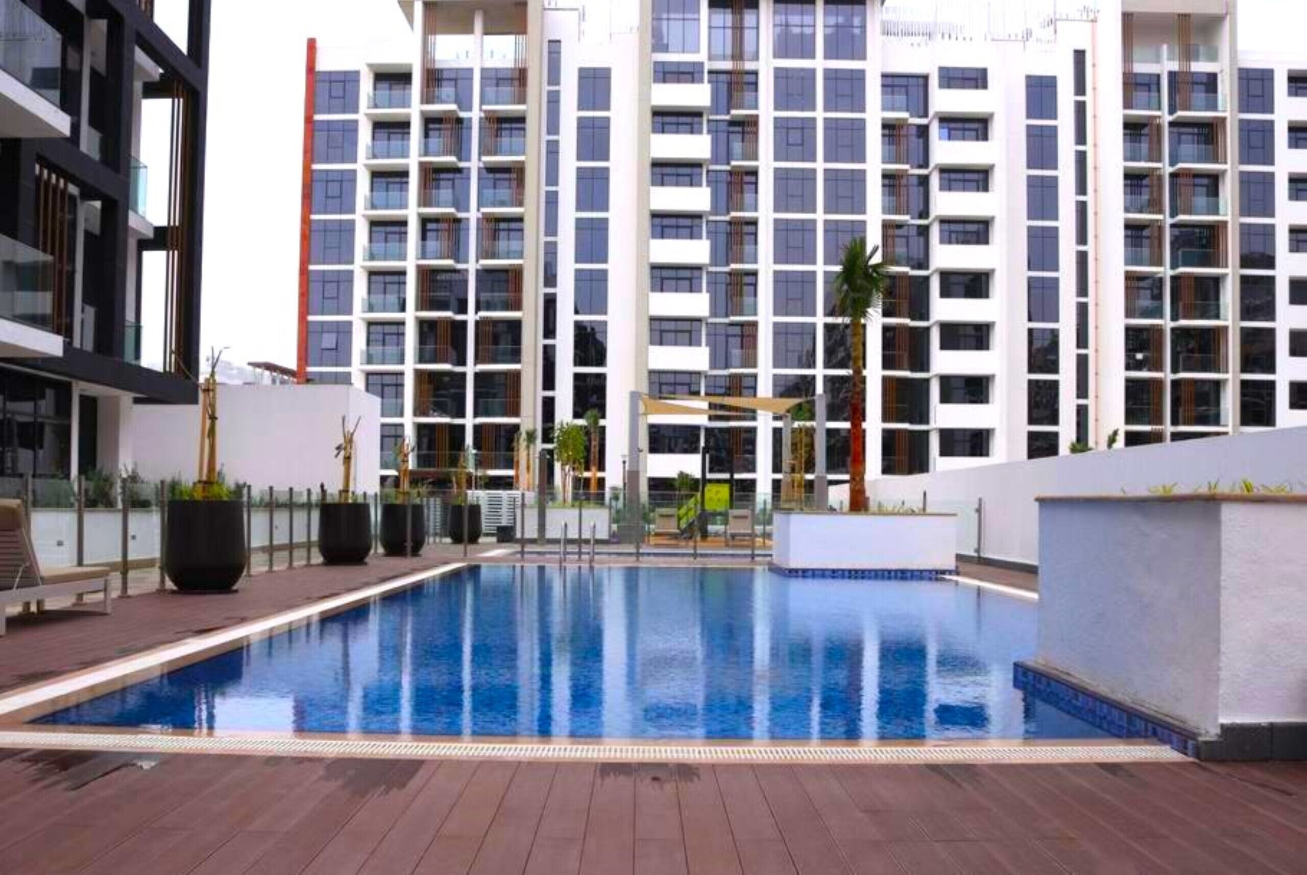Een zwembad met houten terras, omgeven door moderne gebouwen met balkons en grote ramen.