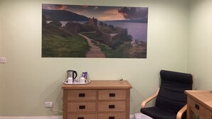 A room with a large landscape painting on the wall, a wooden dresser with a tray of items, and a black chair. - Taigh Sealladh Fèidh B&B (Invergarry)