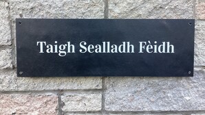 A black sign with white lettering on a stone wall. - Taigh Sealladh Fèidh B&B (Invergarry)