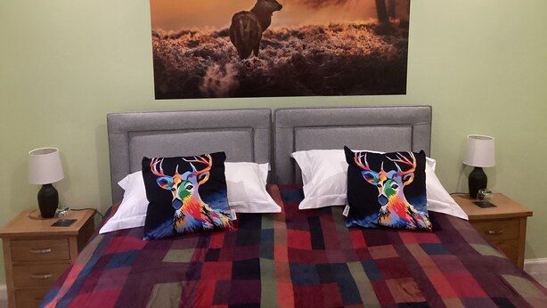 A bedroom with a bed, two nightstands, and a large wall painting of a deer. - Taigh Sealladh Fèidh B&B (Invergarry)